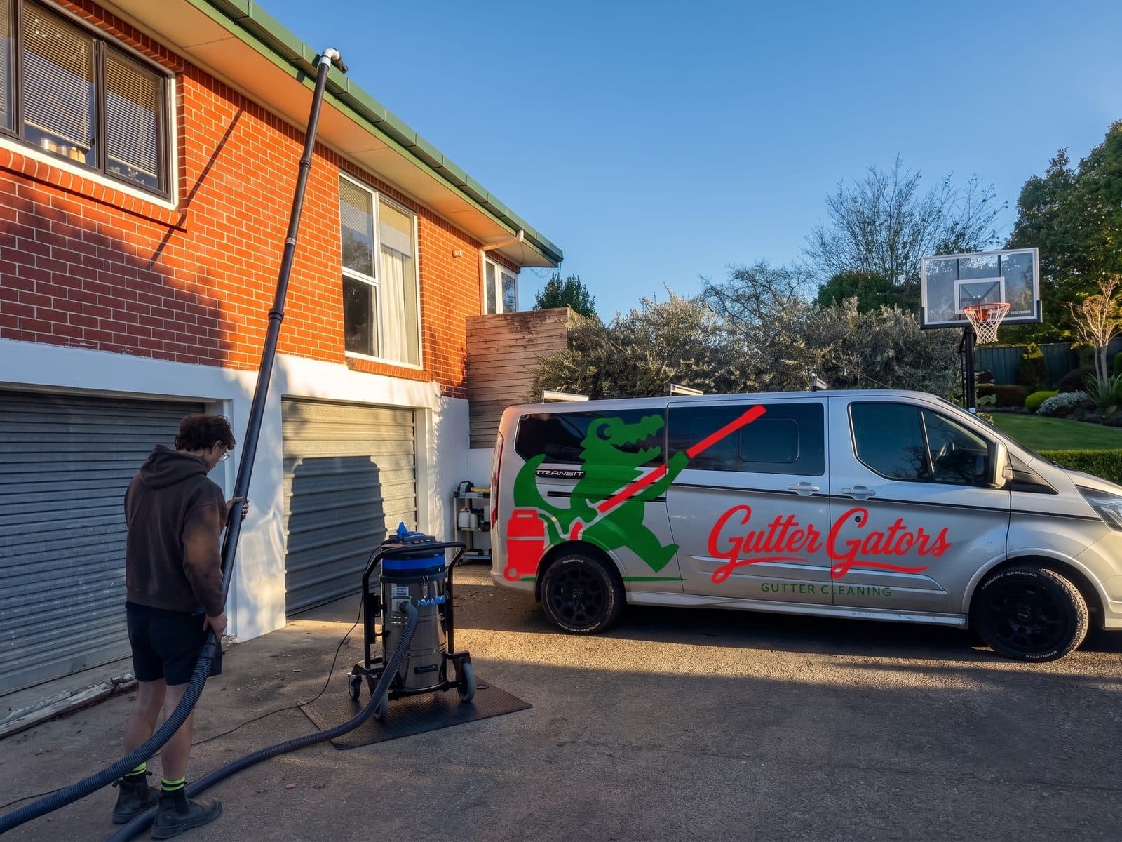 The branded Gutter Gators van at a job — operator clearing a two-storey gutter from the ground with the SkyVac